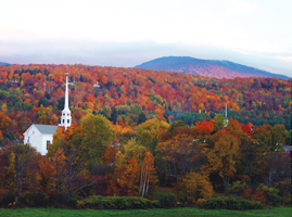 Iconic white church in Stowe Vermont contrasted by red foliage and rolling mountains