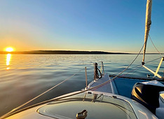 View from the bow of Piper at sunset, capturing vibrant skies and calm waters during a scenic sailing tour.