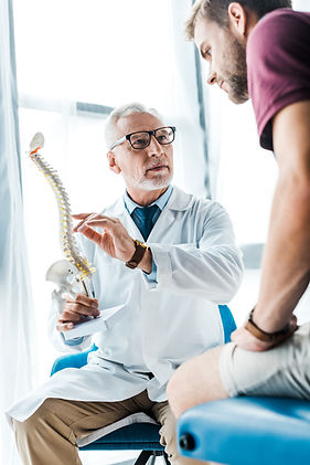 low-angle-view-man-sitting-near-doctor-gesturing-while-holding-spine-model.jpg