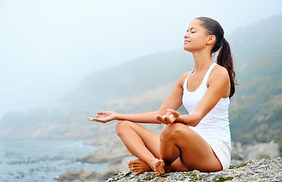 woman meditating on a rock overlooking the beach