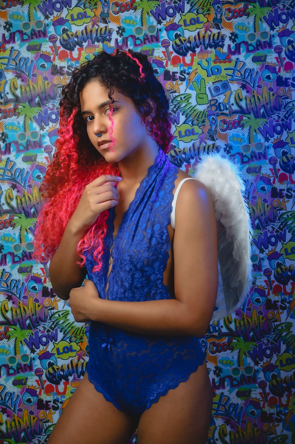 naomi cooper vestida de anjinho com fundo em stiker bomber ela estar de pé com asinhas e uma langerie maiô de renda azul