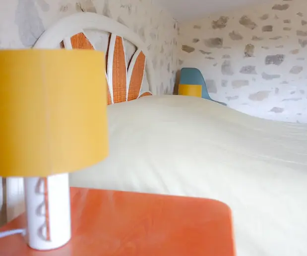 Lampe de chevet jaune près d'un lit dans un chambre aux murs en pierre.