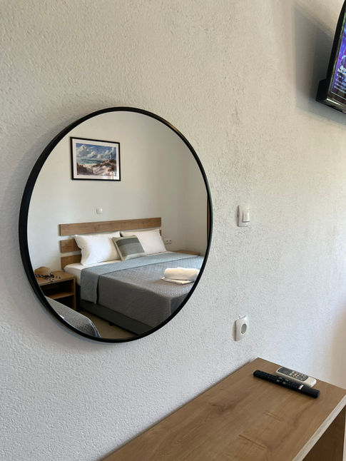Round mirror reflecting bedroom: bed, nightstands