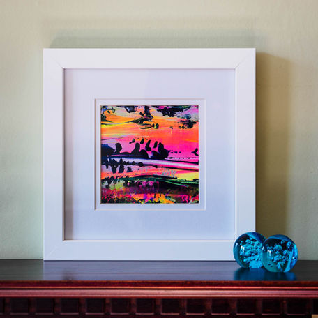Vibrant miniature abstract artwork in a white frame next to two small glass balls.