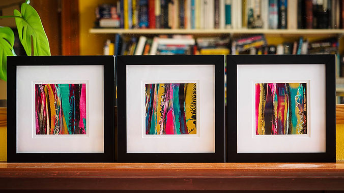 A group of three small framed abstract paintings on a shelf