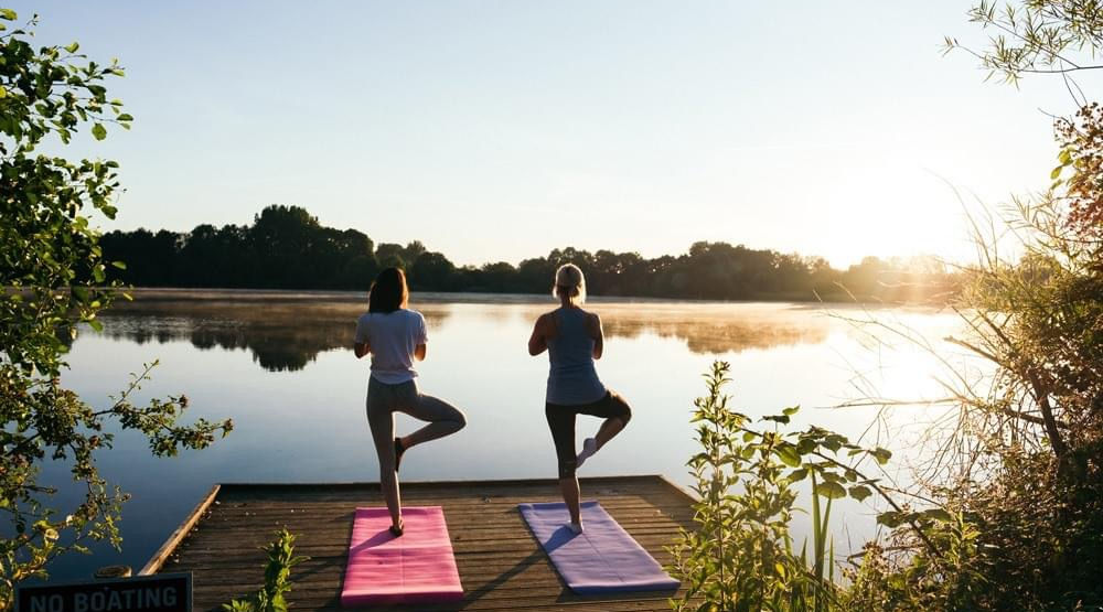 Two ladies practicing yoga by a lake