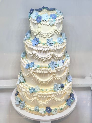 Four-tier vintage wedding cake with ivory buttercream and clusters of blue buttercream flowers in varying shades