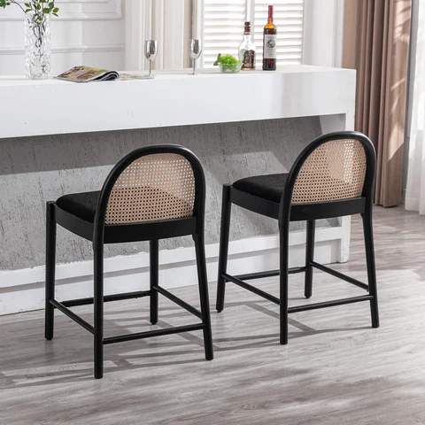 Two black rattan chairs at a modern white bar with bottles, glasses, and a book. Bright room with wooden floor and neutral tones.