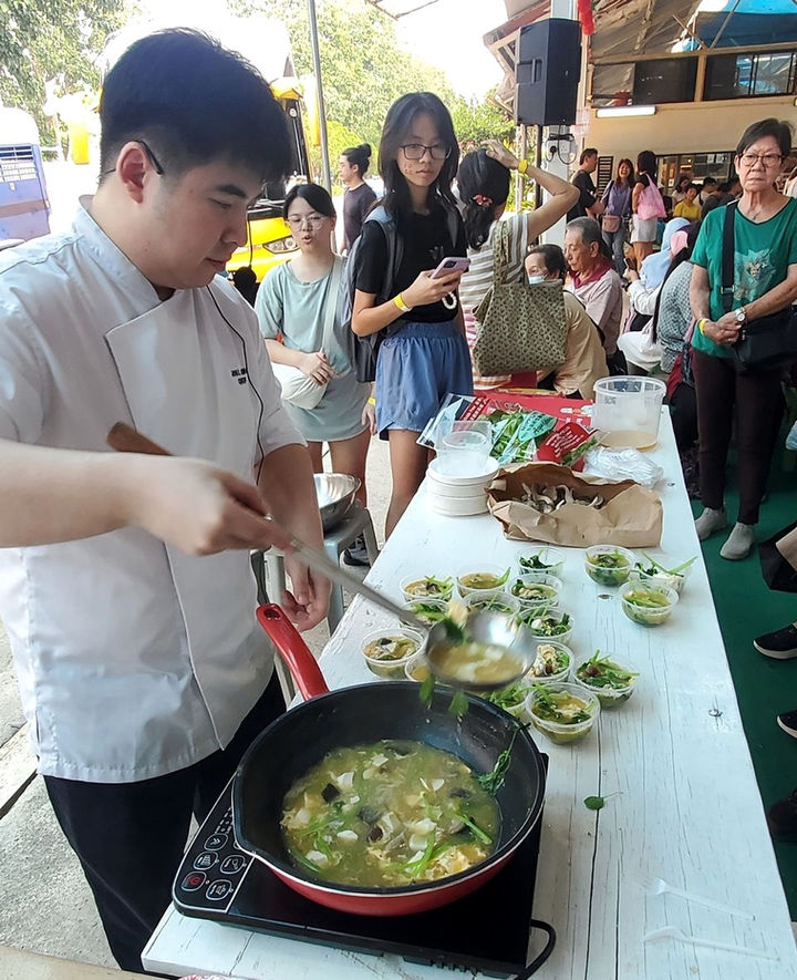 Chef Joel Ong ladling food into tasting cups as visitors watch a cooking demonstration