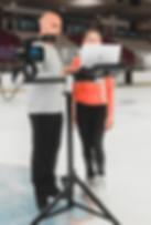 A figure skating coach talks on the ice with a skater with a video analysis system, a vide camera and a computer