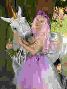 Milo the Unicorn Smiles for a photograph next to a woman wearing a purple and green fairy costume.
