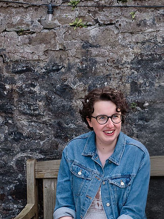 Photo of Emma, a white woman, sat on a bench in a denim jacket and smiling