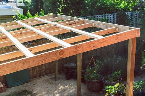 under construction garden pergola with wooden structure in sunny backyard surrounded by tr