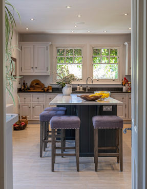 Modern fitted kitchen at Kingswood Avenue, Queen's Park, with a central island, bar stools, and recessed lighting in a bright, open-plan space