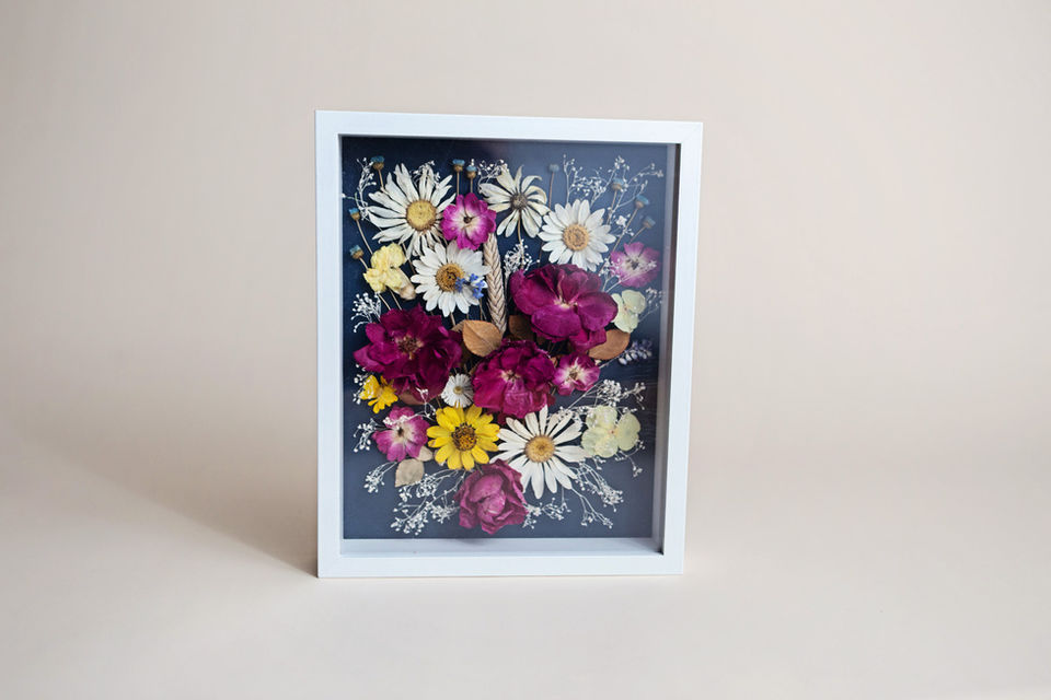 Floral arrangement in a white frame, with dark background, daisies and roses.