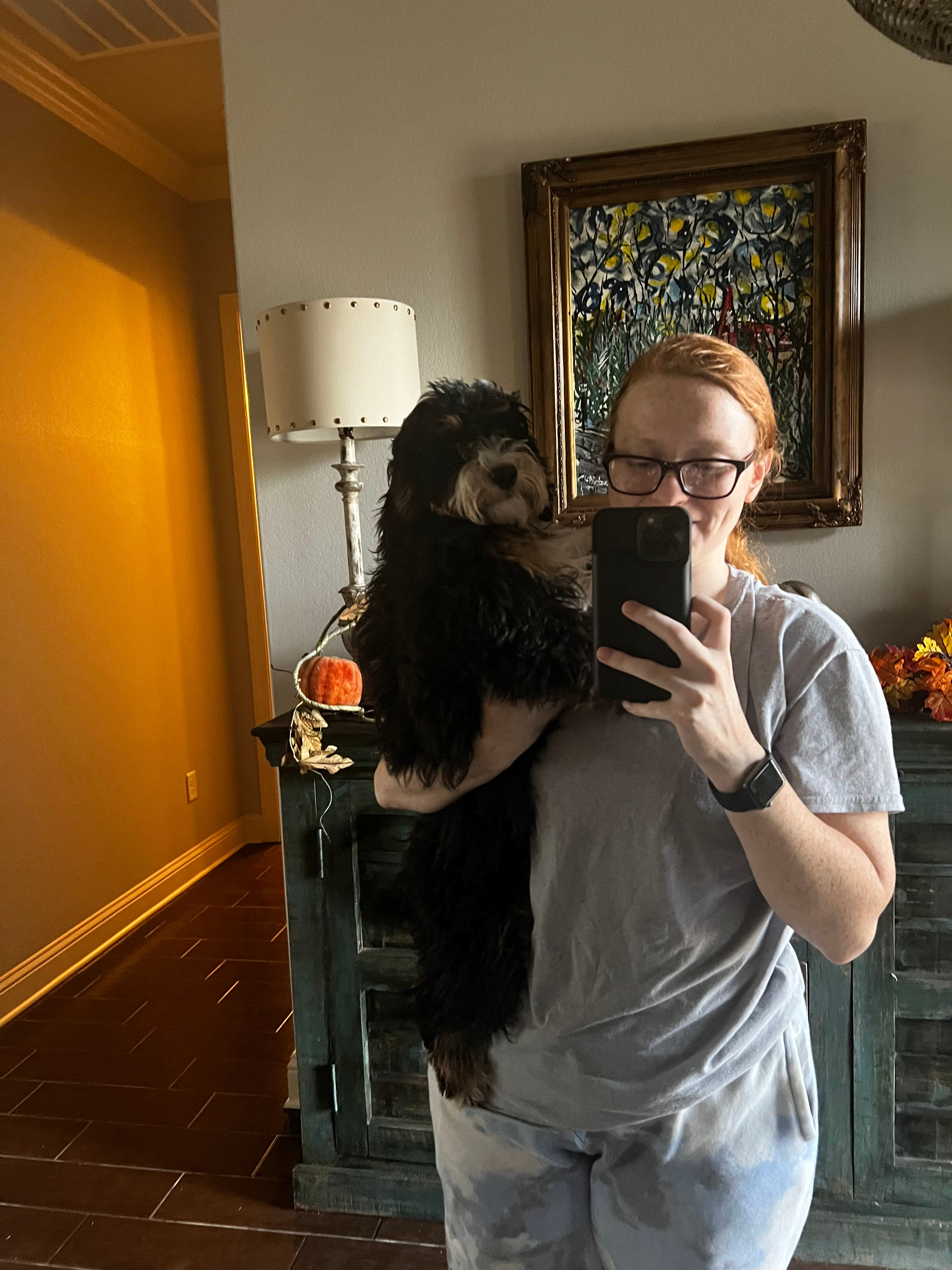 Girl talking picture in mirror with a doodle dog sitting on her hip like a toddler