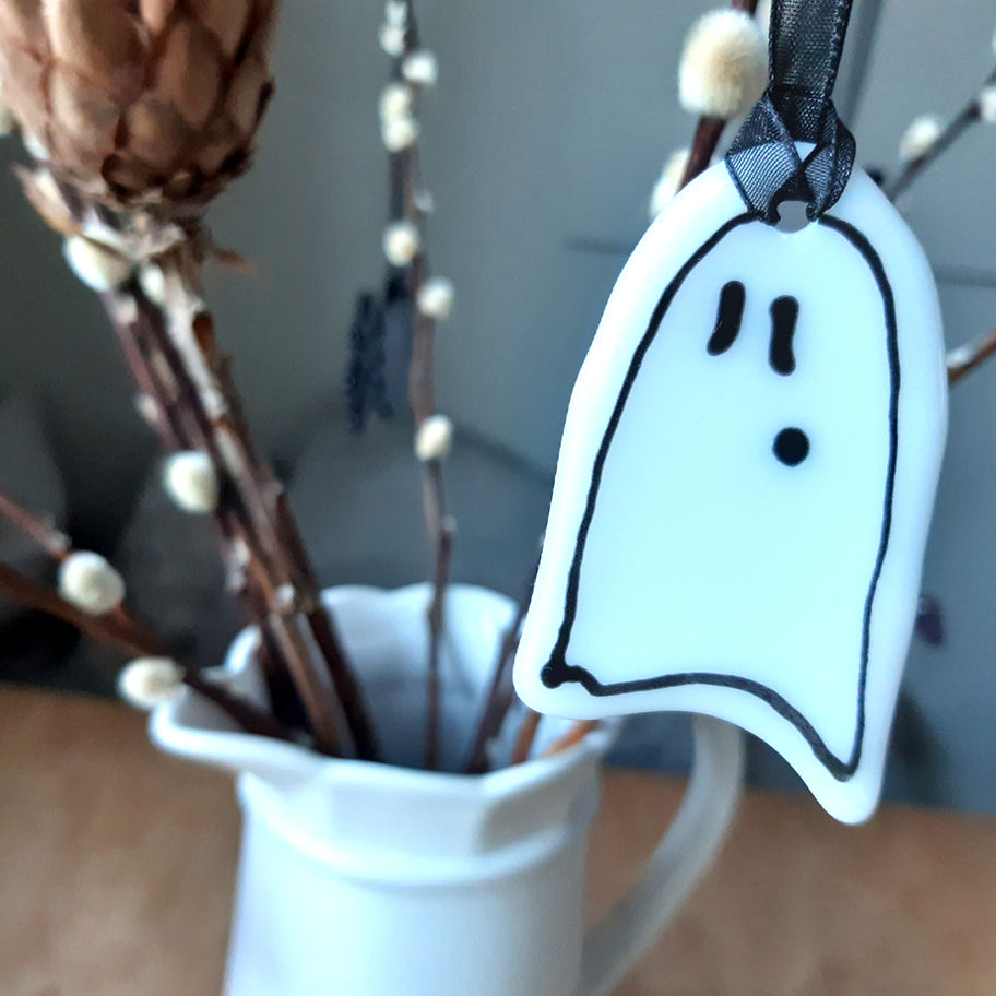 White ghost fused glass decoration hanging in a white vase with branches and flowers.