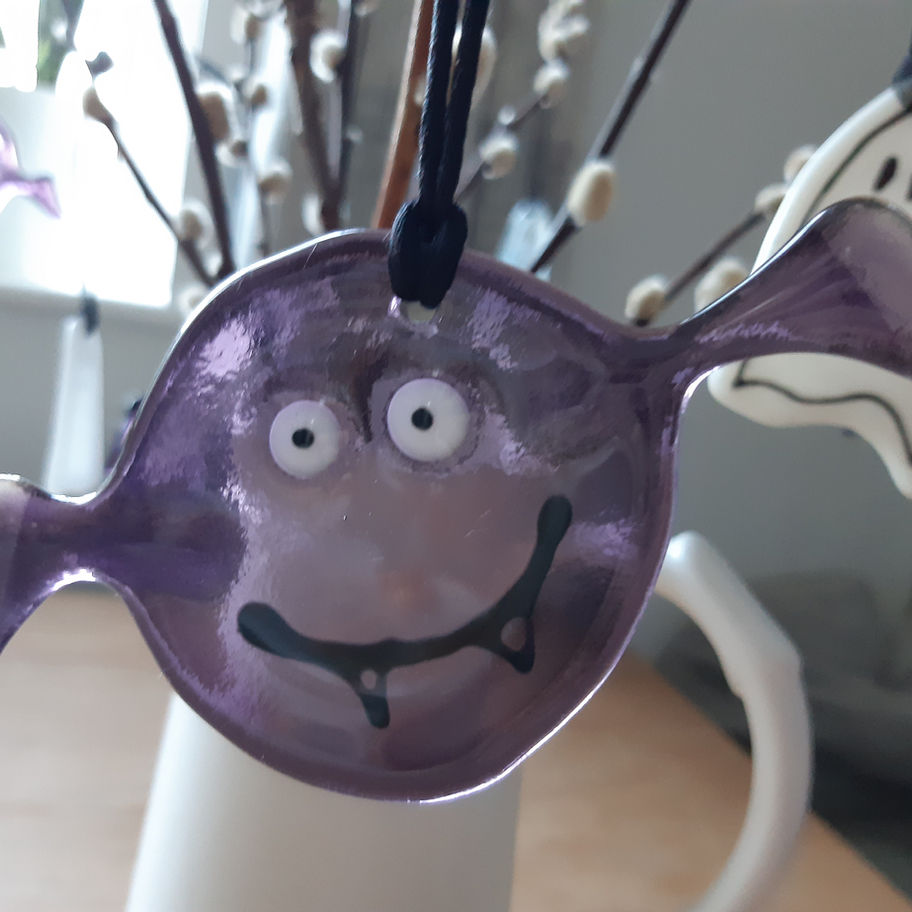 Purple glass art with eyes and smile, Tam's Glass, in front of flowers.