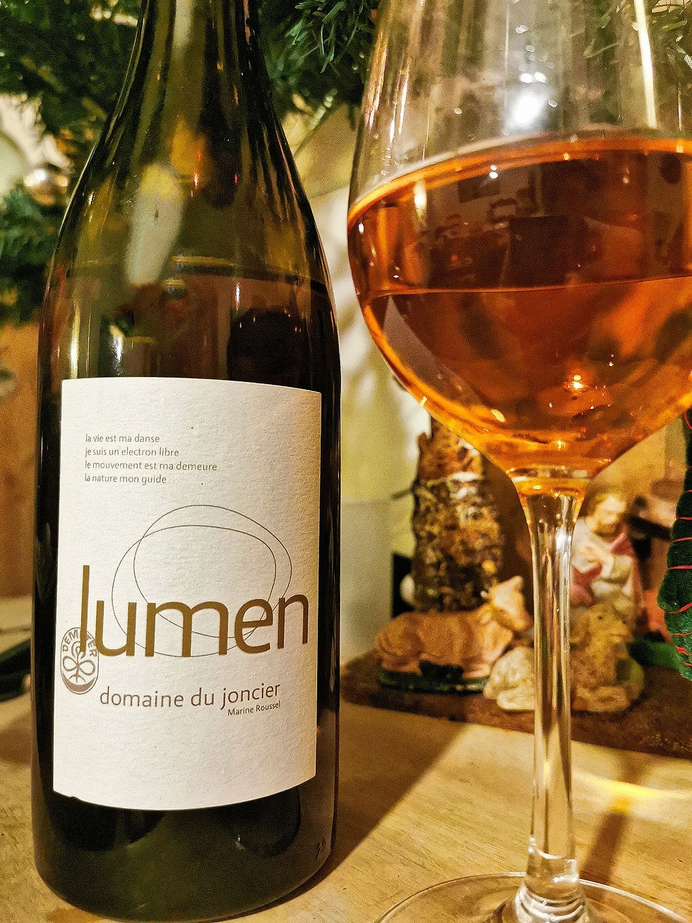 On y voit une bouteille de vin blanc qui se nomme Lumen. Un verre rempli. la couleur du vin est orange. dans le fond, un sapin et une crèche