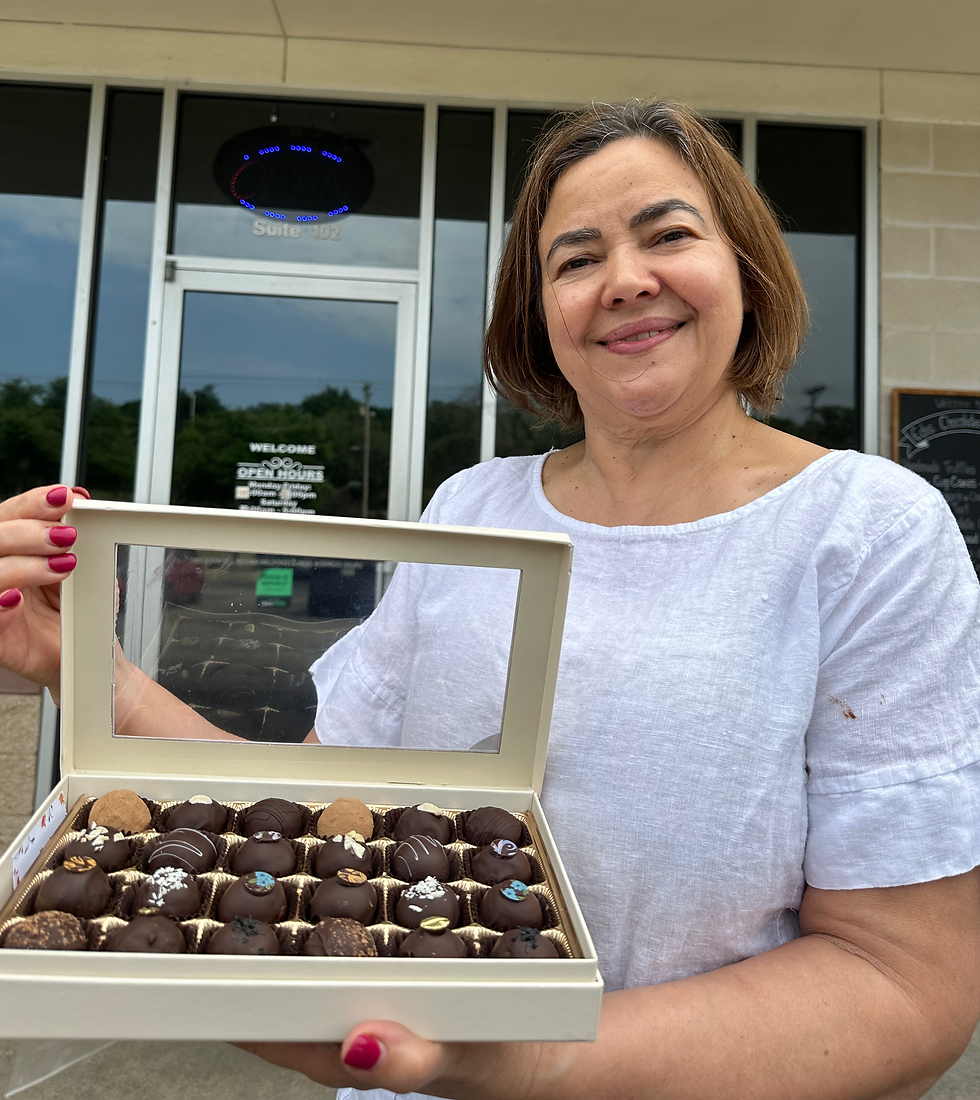 Edis Rezende standing in front of her bakery while holding a box of chocolate truffles.