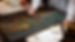 A person meticulously restores a painting using a brush. The setting is a worktable with jars and a palette. The atmosphere is focused.