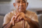 A seniro man sitting down holding a cane with an emotionless expression. 