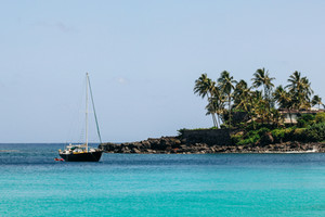 Sail boat anchored in turquoise water near tropical coastline. 