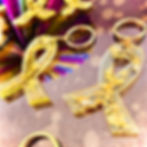 Porte-clés artisanal en résine jaune transparente avec paillettes et feuilles d'or, forme ruban de l'endométriose.