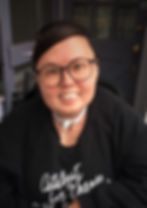 Stacey Milbern has short hair and round glasses. They are smiling at the camera, and wearing a black sweater with white text: Catalyst for Change
