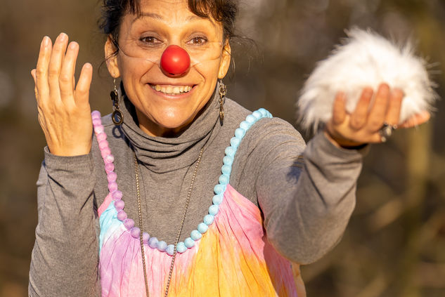 Lächelnde Clownsfrau mit roter Nase zeigt weißen Flaum