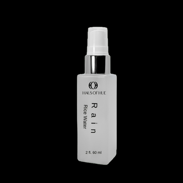 A sleek white bottle labeled "HAUS OF HUE Rain Rice Water" with a silver pump cap. The product is displayed against a solid black background, emphasizing a minimalist and modern design.