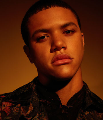 Sepia-toned close-up portrait of a young man with a calm expression, illuminated by warm, beautiful light.