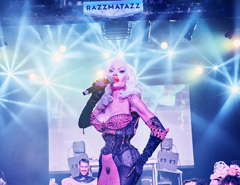 Amanda Lepore standing on stage at IAMICONIQA surrounded by joyful queer humans celebrating diversity.  