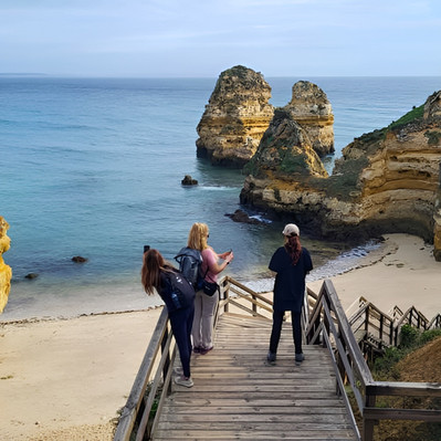 תיירים יורדים במדרגות עץ לחוף פראיה דו קאמילו עם תצורות סלע גיר מרשימות באלגארבה פורטוגל