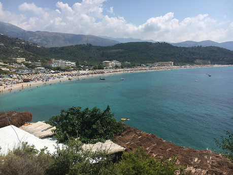 Livadhi Beach on the Albanian Riviera near Himara, known for its pristine blue water, beach umbrellas, and scenic mountain views