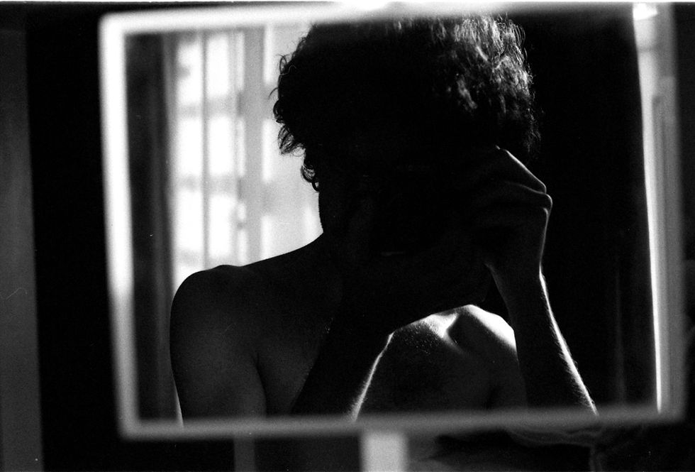 Silhouetted person reflects in mirror, stark black and white lighting.