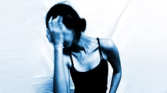 A person in a black tank top holds their head in distress against a white background. The image has a blue tint, conveying a somber mood.