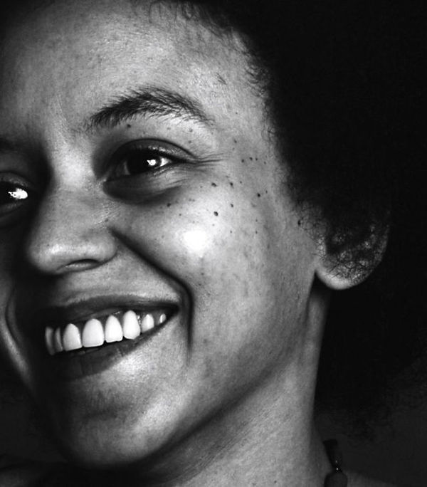 Poet Nikki Giovanni is smiling while looking away from the camera. She is pictured from the neck up in a black and white photograph.