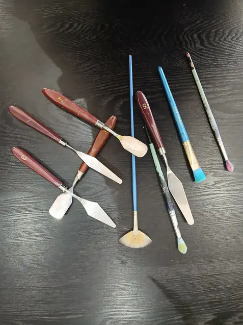 Assortment of palette knives and paintbrushes on a dark table