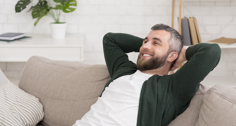 Man lays on sofa with hands behind back.