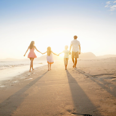 A mother and father walking into the sunset on a beach while hand-in-hand with their two children between them.