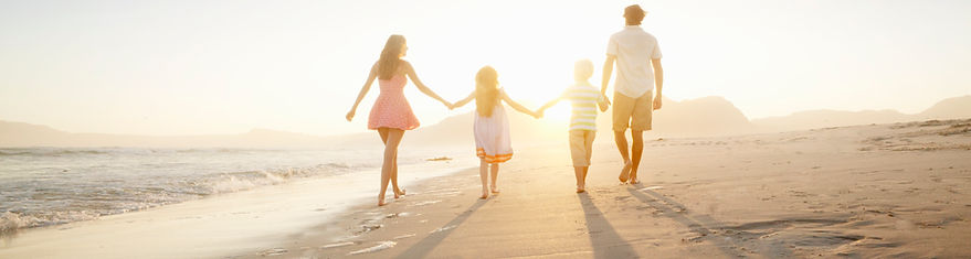 Family of four walking on a beach into a sunset