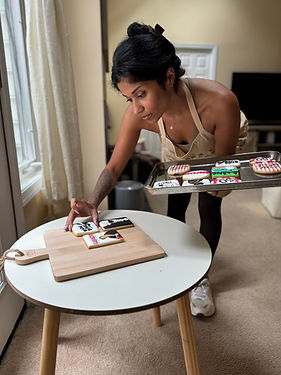 Woman placing decorated cookies from baking sheet onto wooden board.