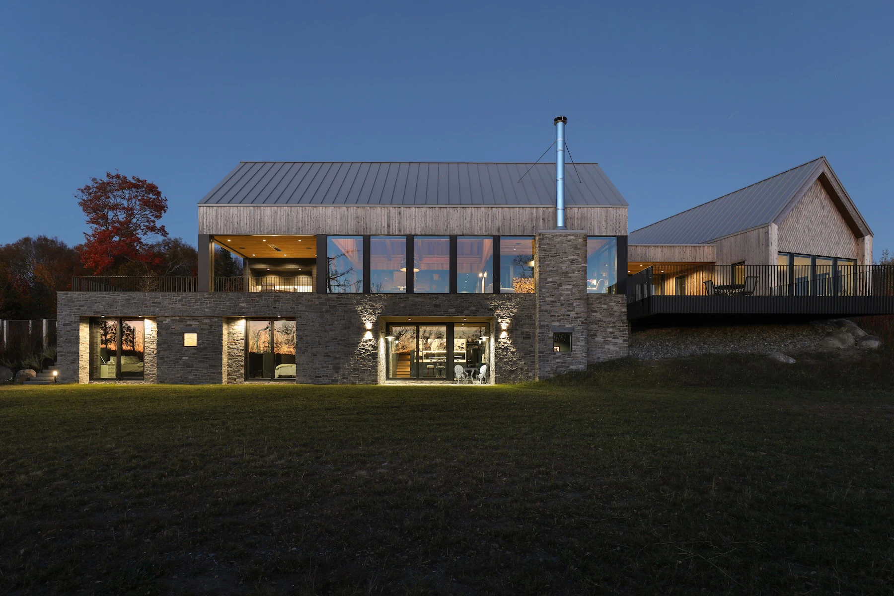 Complete view of rear exterior of Rivers Edge Homestead, overlooking patio with the sunset visible in Marvin windows reflection