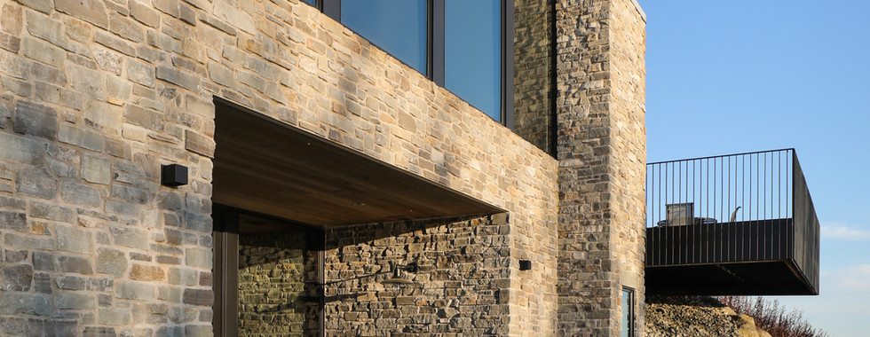 Lower level entrance surrounded by stone with large wall of Marvin windows above in the main level.
