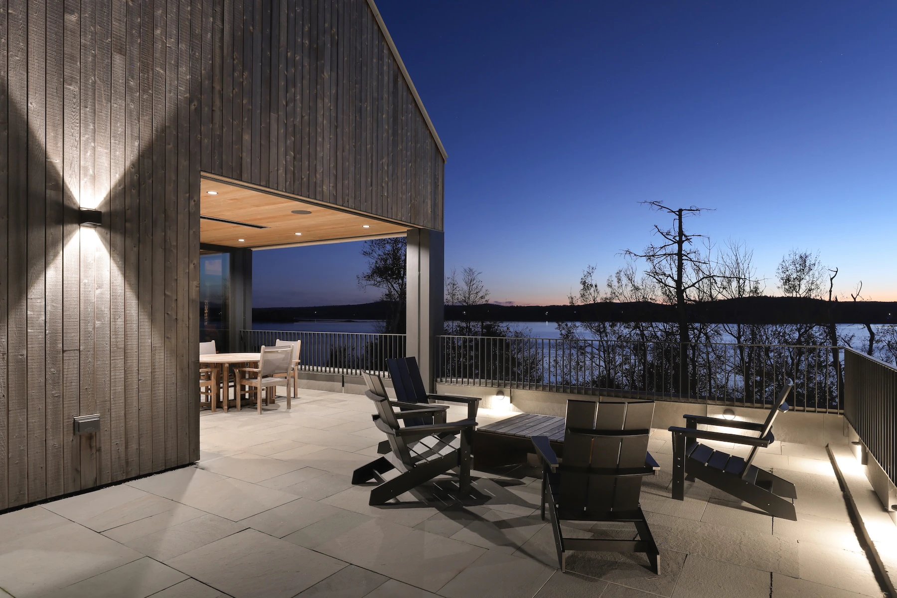 Last minutes of sunlight barely visible in the distance on the horizon with an illuminated patio space with fireplace and covered dining area