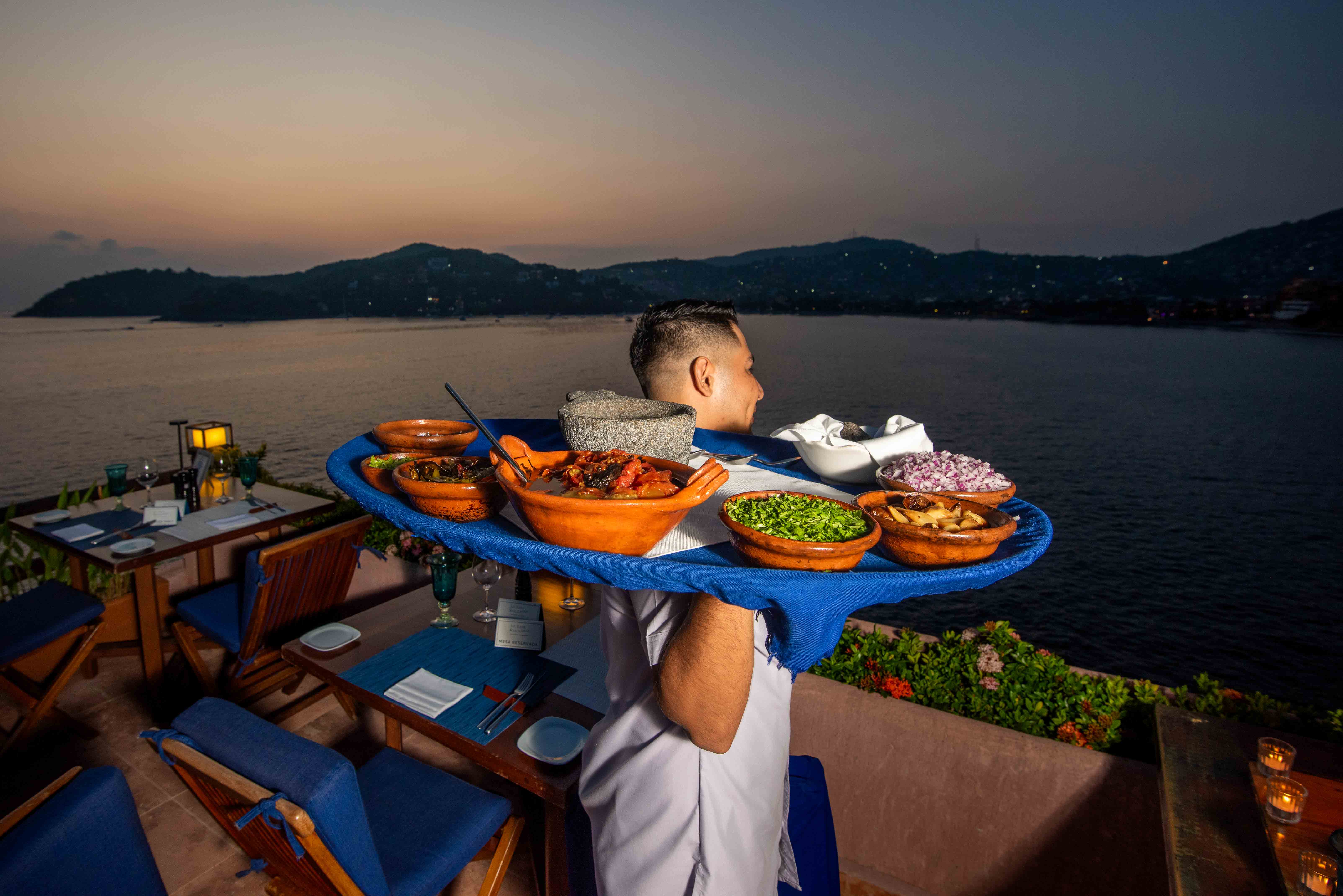 Waiter carrying dinner on a tray across the sunset terrace at La Casa Que Canta