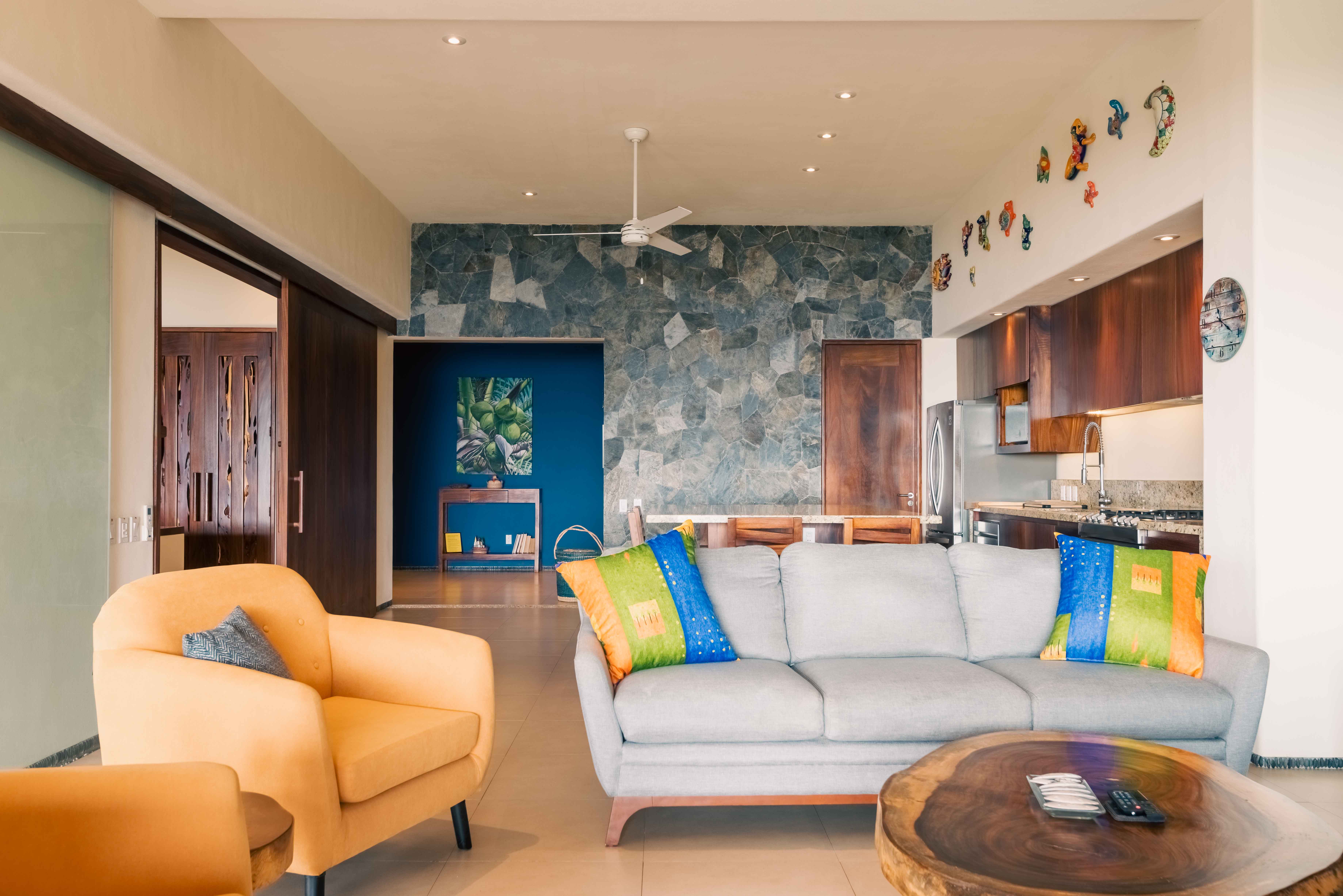 Colorful living room with parota wood table, stone walls, kitchen and custom woodwork