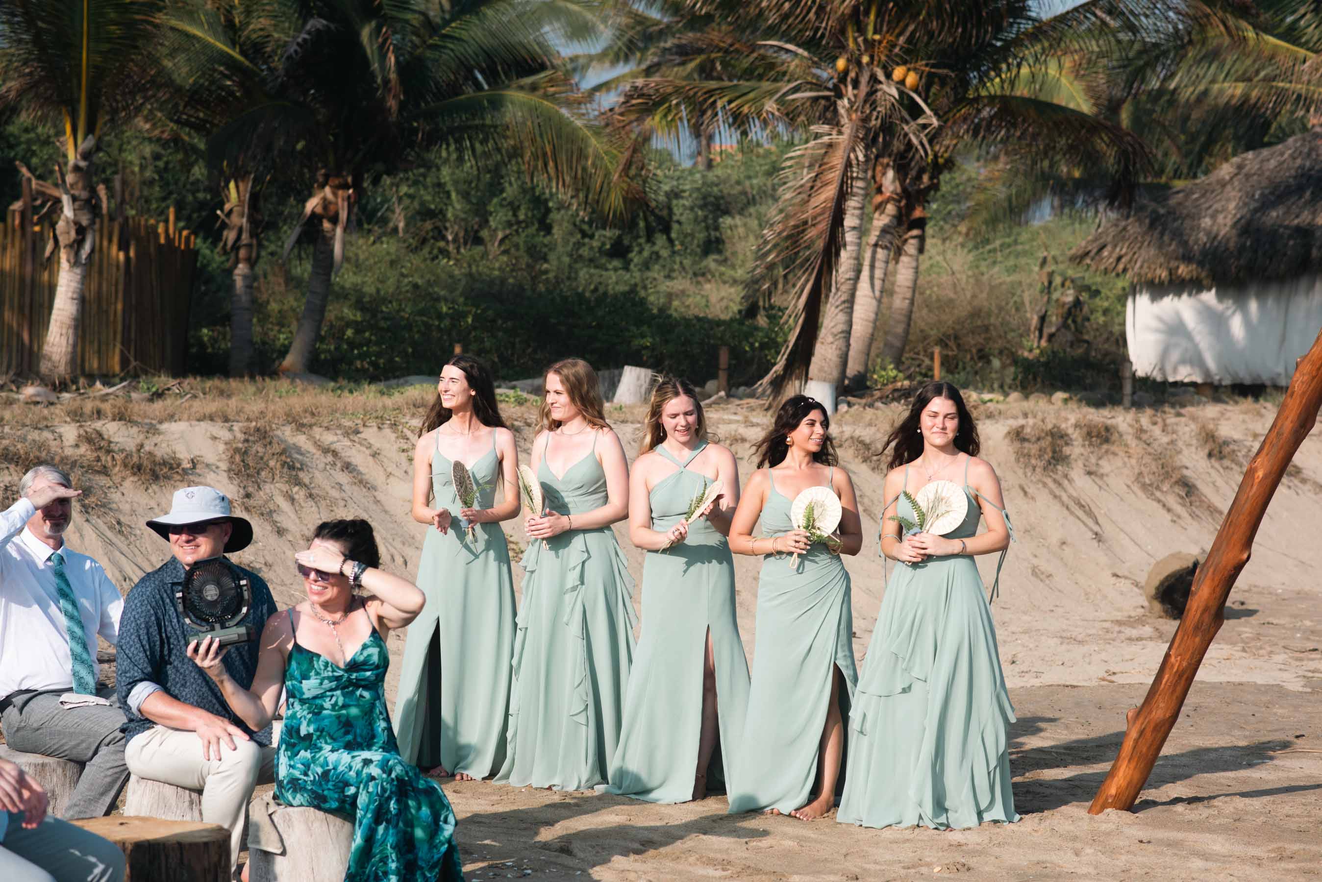 Bridal party walking along Playa Viva beach in neutral, natural-toned dresses
