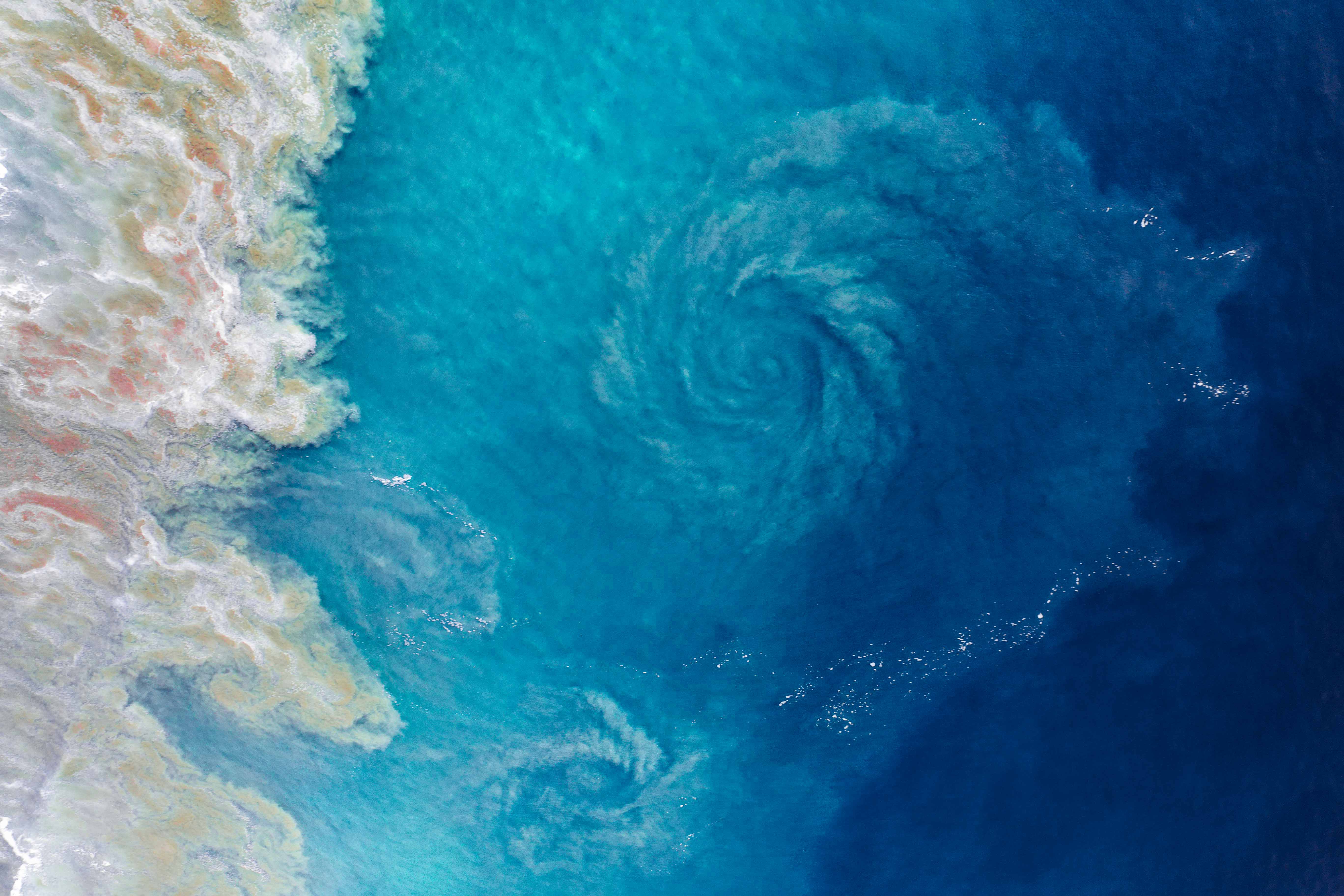Top-down aerial view of ocean whirlpool with spiral sand pattern and deep blue Pacific waters in Mexico